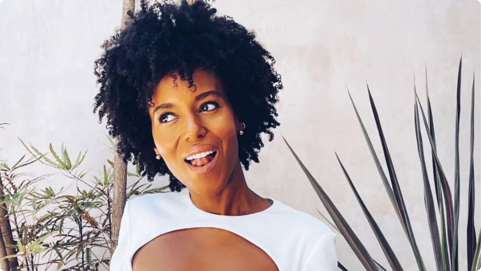 Close-up of Kerry Washington showcasing defined natural curls and radiant makeup with green plants