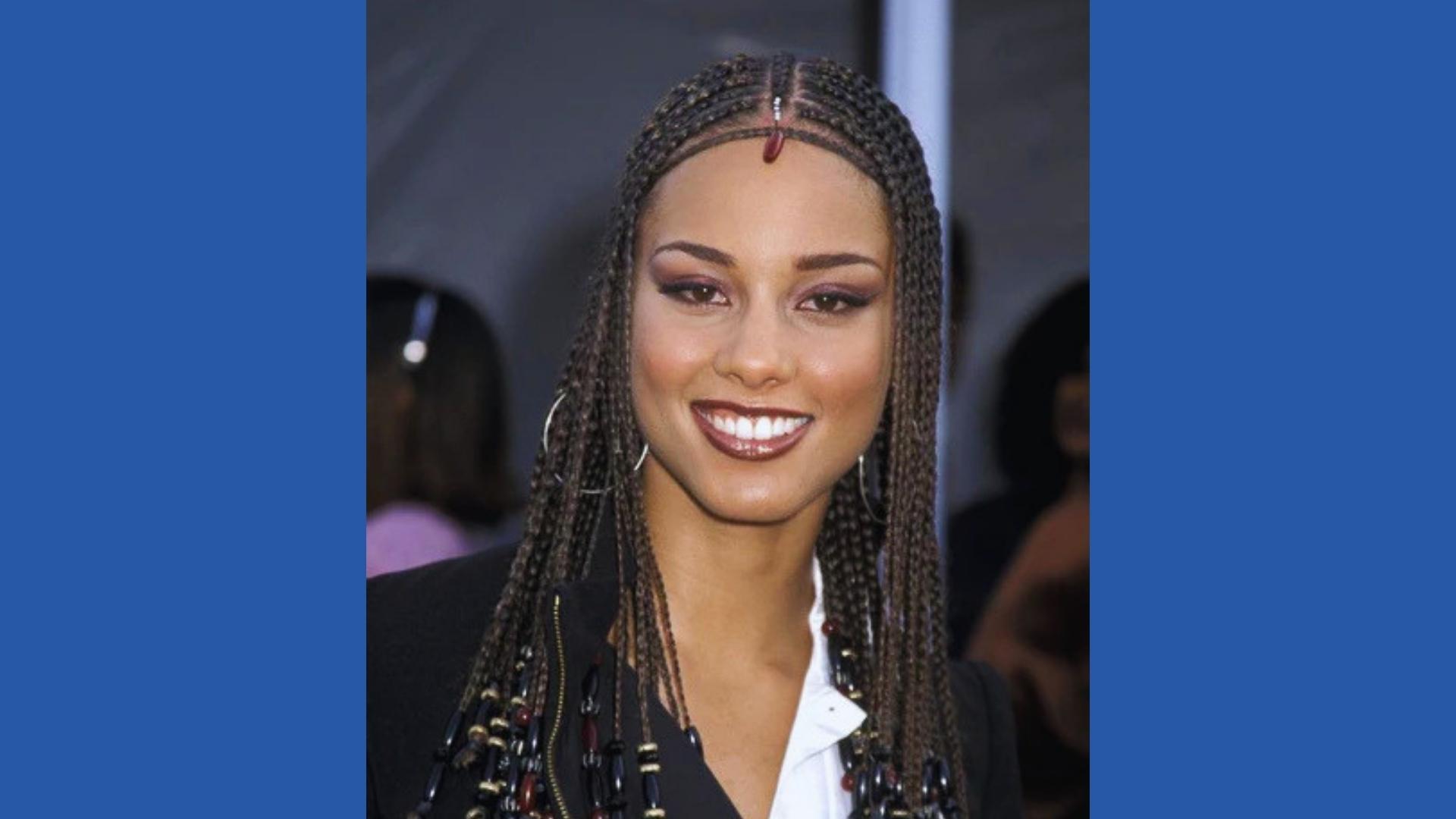 Young Alicia Keys smiles with signature beaded micro braids, center part, jeweled hair accessory, black blazer, hoop earrings.