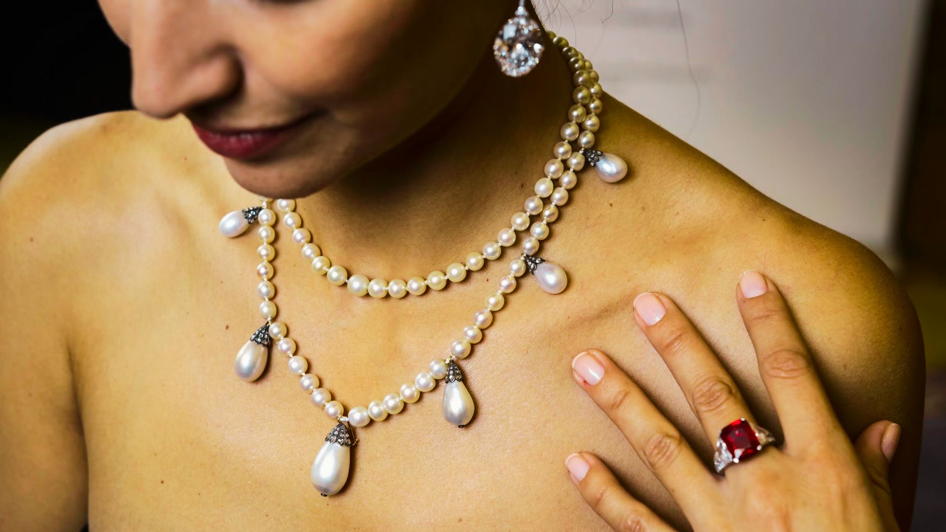 Close-up of layered vintage pearl necklaces with teardrop pendants, paired with a bold ruby ring.
