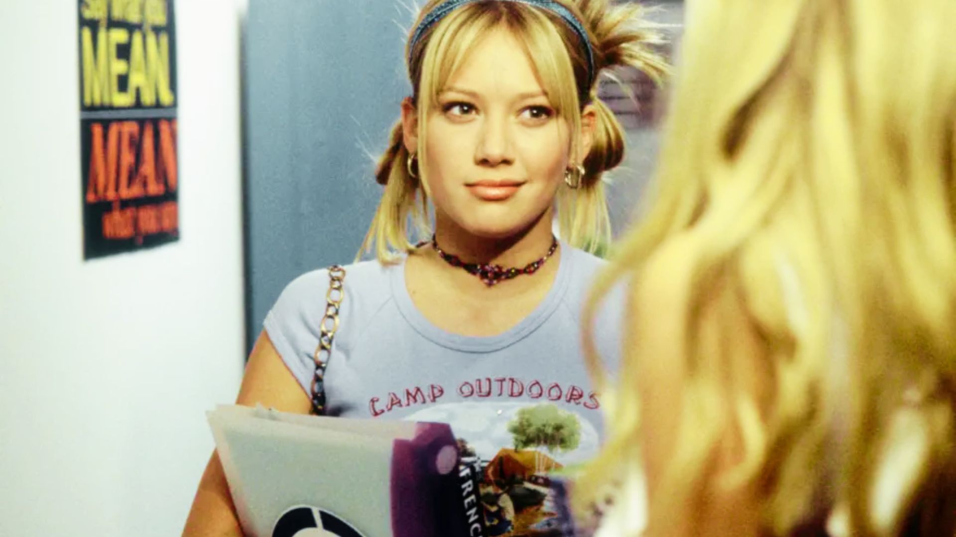 Young Hilary Duff as Lizzie McGuire wears a light blue “Camp Outdoors” baby tee and beaded choker.