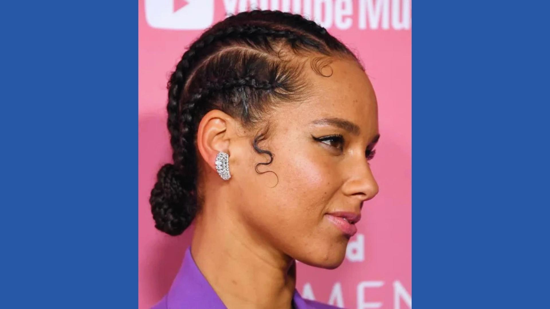 Profile of Alicia Keys with sleek cornrows into low braided bun, baby hairs styled, diamond ear cuff, purple blazer, pink backdrop.