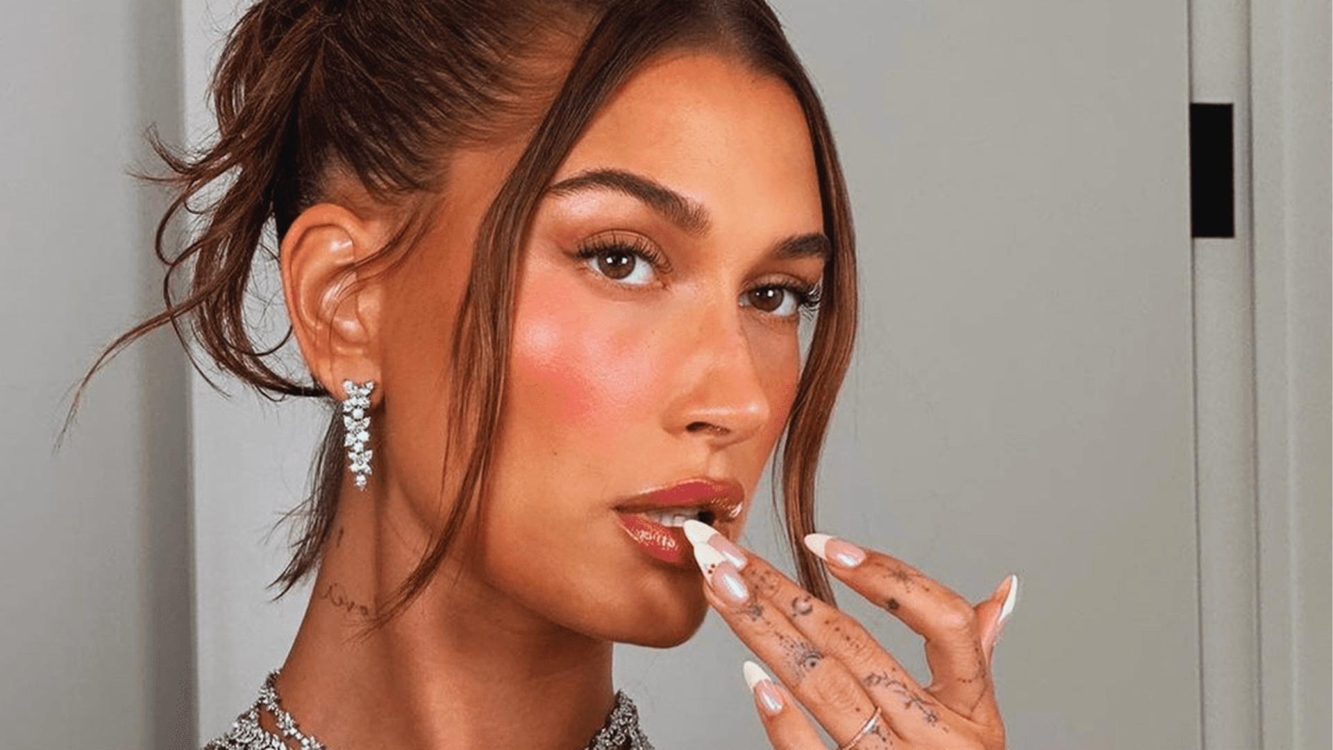 Close-up of hand with short rounded nails in Hailey’s signature glazed donut chrome over sheer nude, diamond ring on finger.