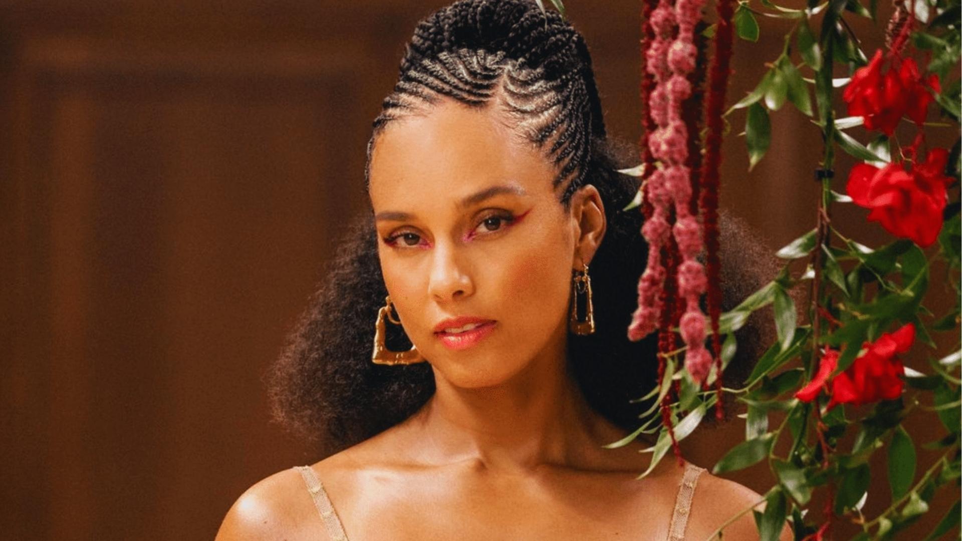 Alicia Keys wears cornrows pulled into high braided mohawk with natural curly ponytail, gold earrings, soft glam, floral backdrop.