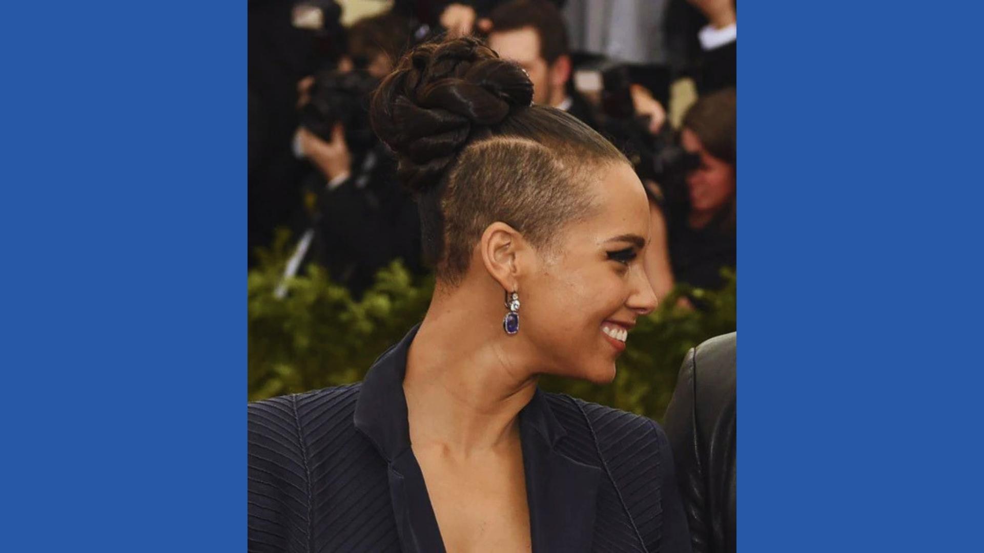 Alicia Keys smiles at Met Gala with edgy braided top knot, shaved undercut sides, and sapphire earrings in black blazer.