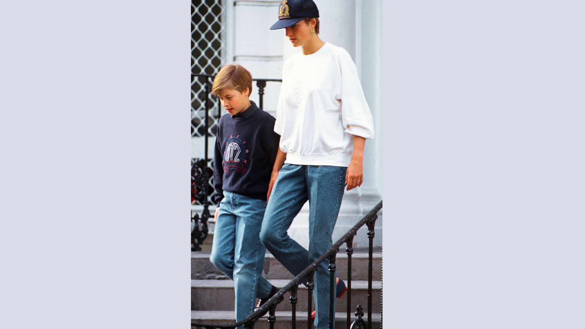 Princess Diana walks down steps with Prince William in matching casual denim and sweatshirts.