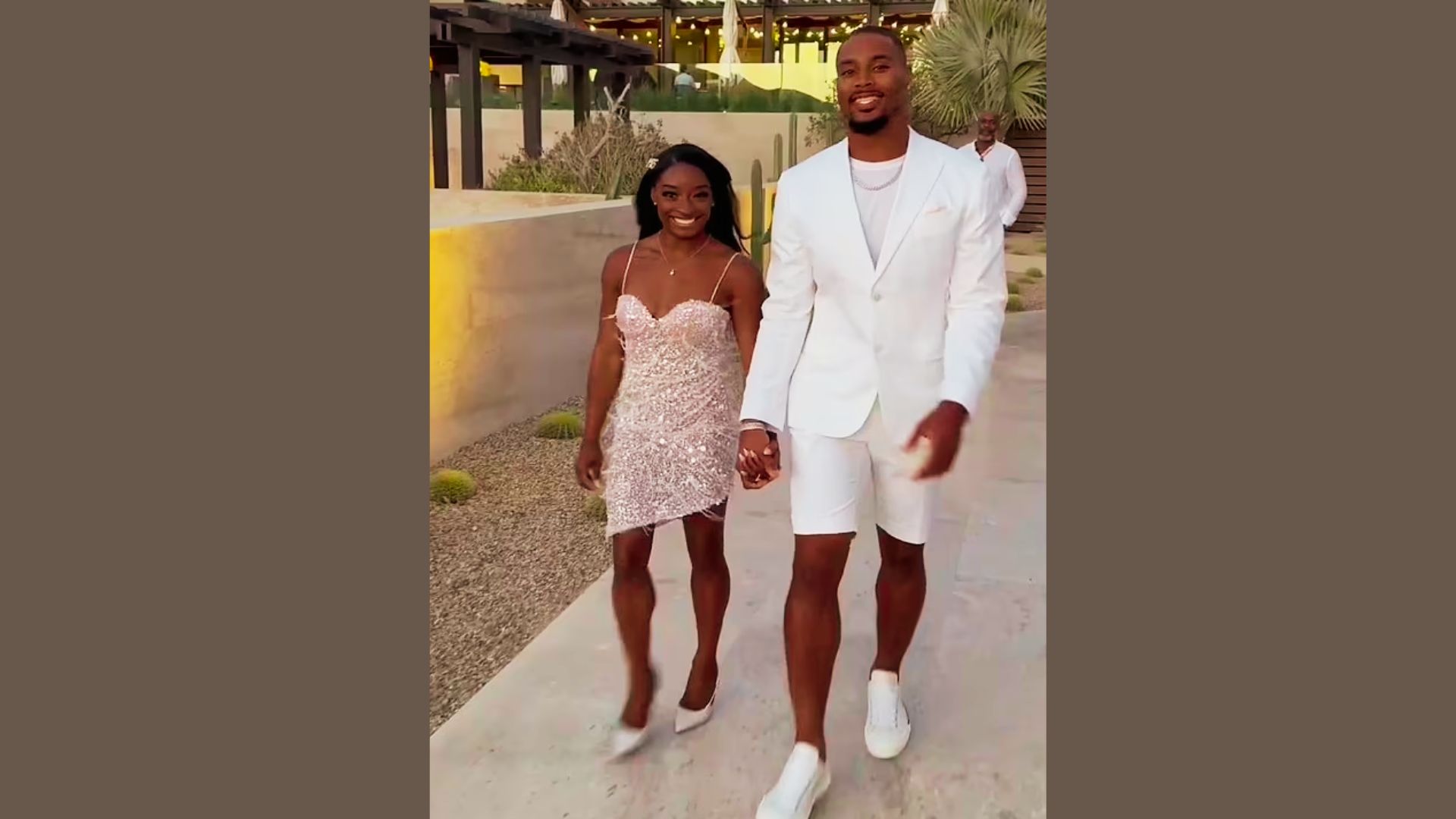 Simone Biles and husband Jonathan Owens walk hand in hand outdoors at their wedding rehearsal.