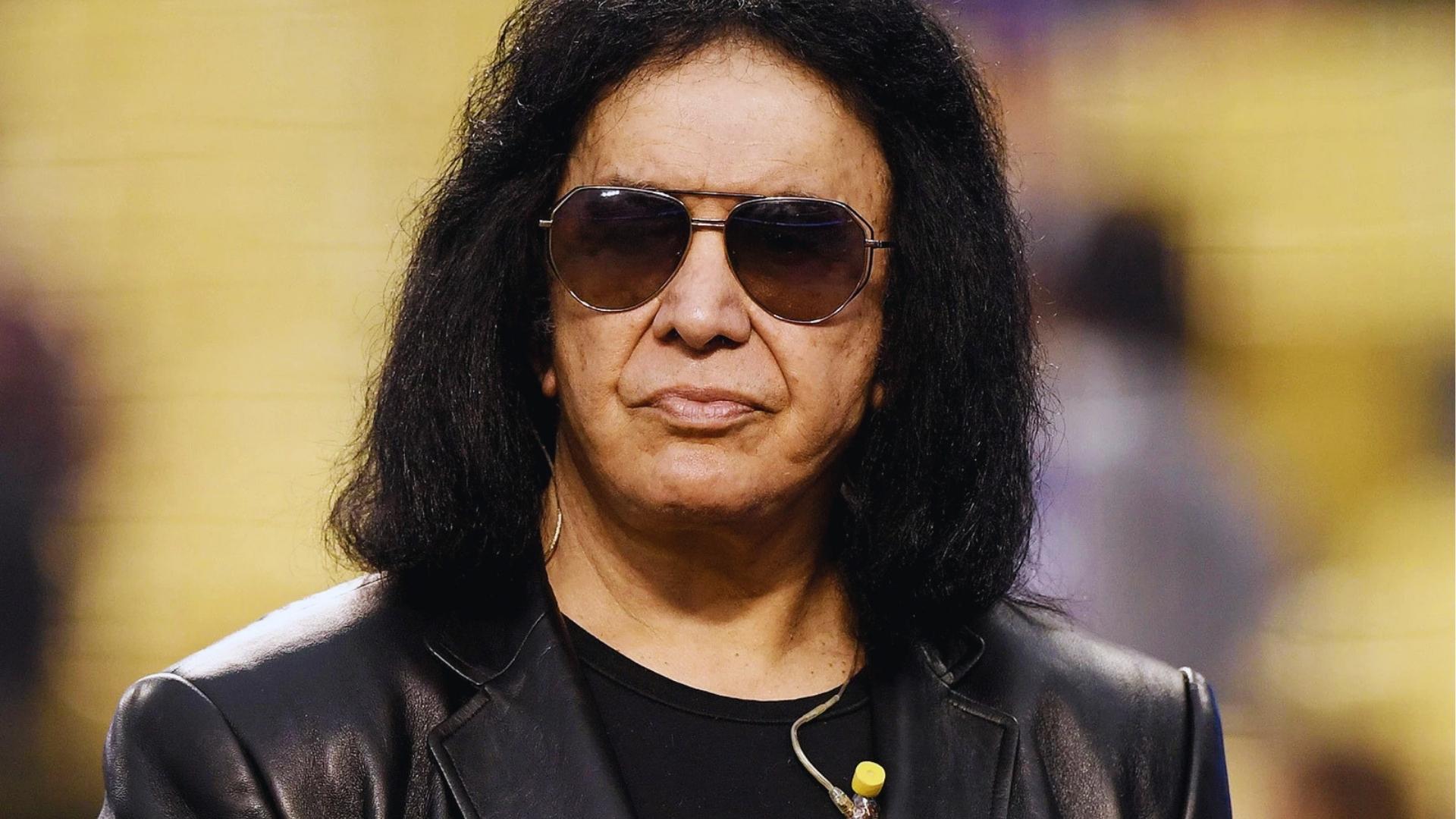 Gene Simmons without stage makeup wears aviator sunglasses and black leather jacket, long curly hair, at public appearance.