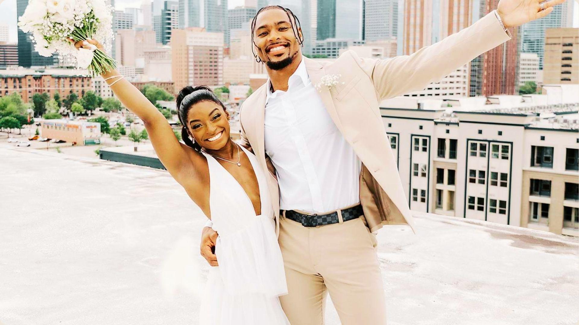 Simone Biles and Jonathan Owens celebrate on a rooftop with a city skyline behind them.