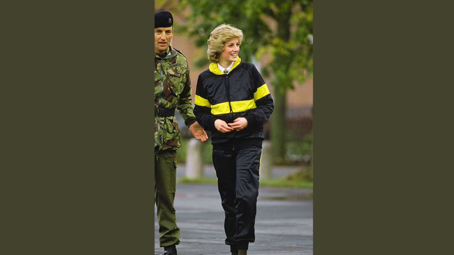 Princess Diana laughs while walking outdoors in a black and yellow striped tracksuit.