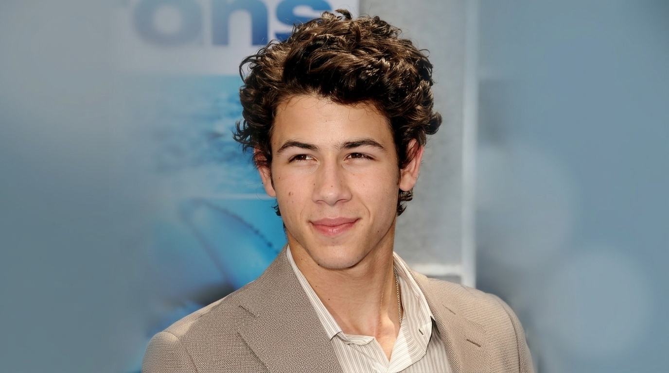 Nick Jonas smiling with short curly quiff hairstyle in beige suit