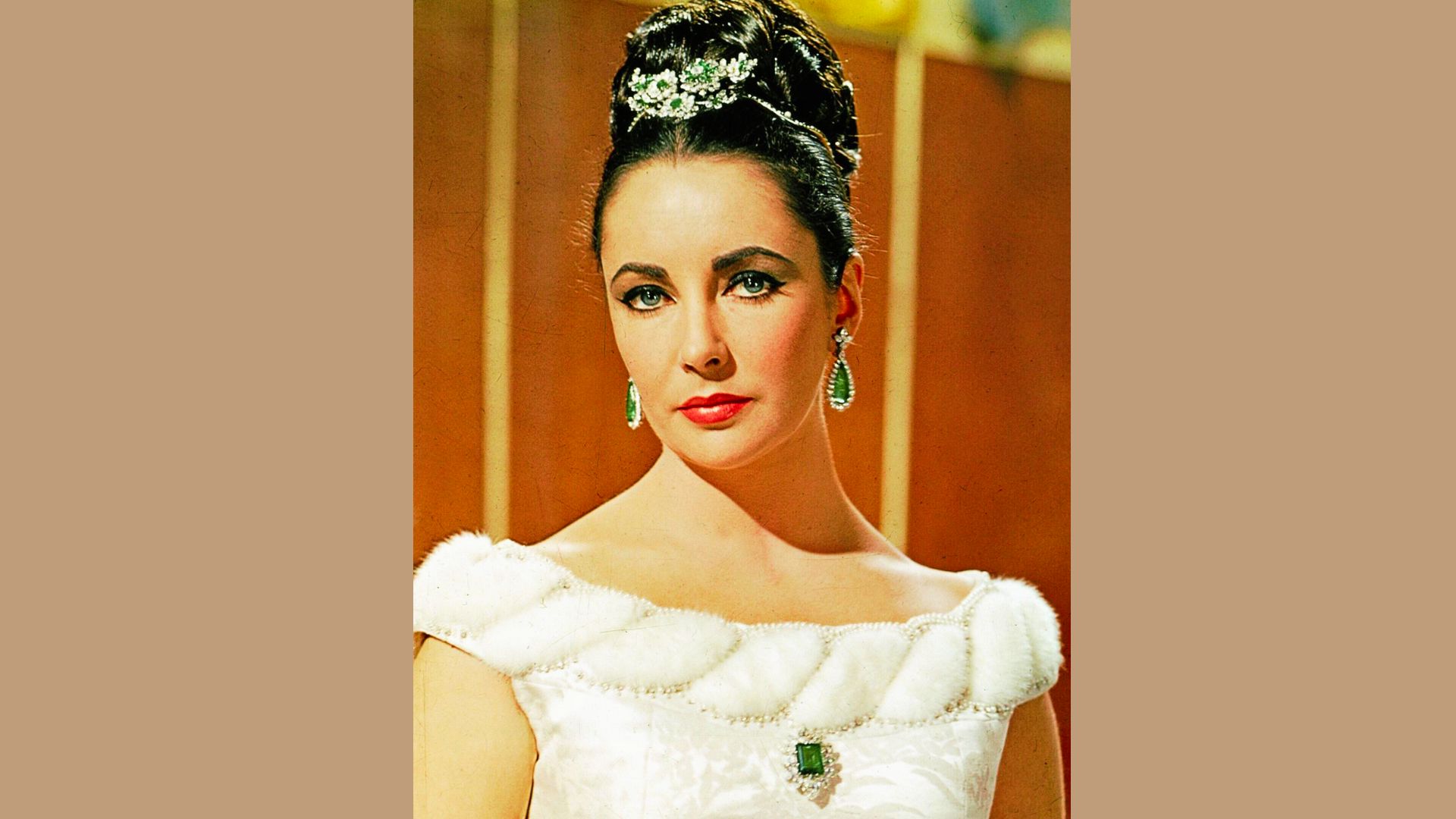Portrait of Elizabeth Taylor in a white fur-trimmed gown with emerald jewelry and an ornate updo.
