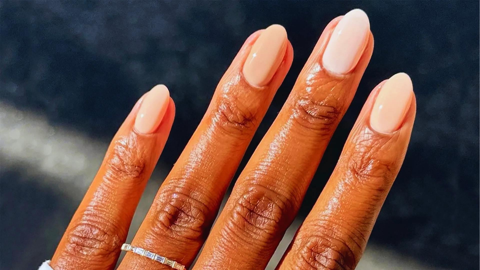Hands with almond-shaped nails in pearly glazed donut finish, chrome sheen catching light, paired with rings and mesh sleeve.