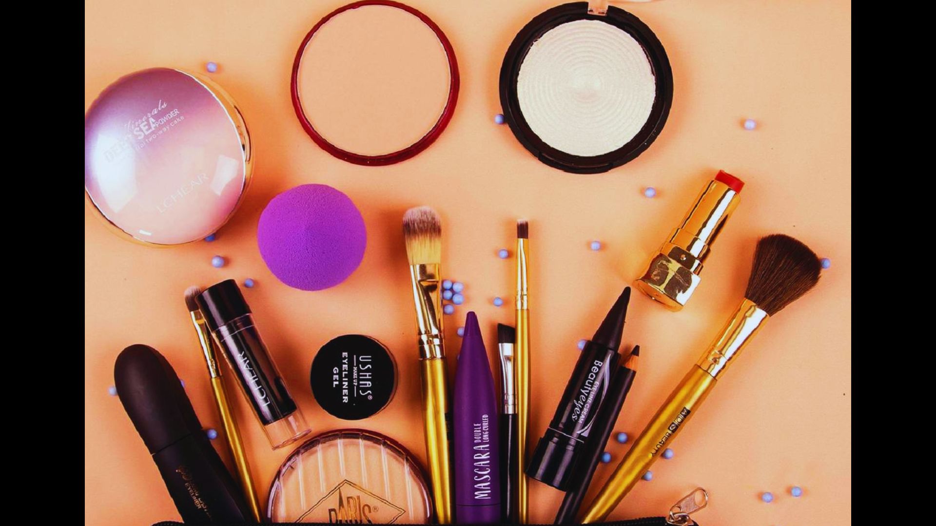 Flat lay of various makeup products including brushes, mascara, eyeliner, lipstick, and setting powder.