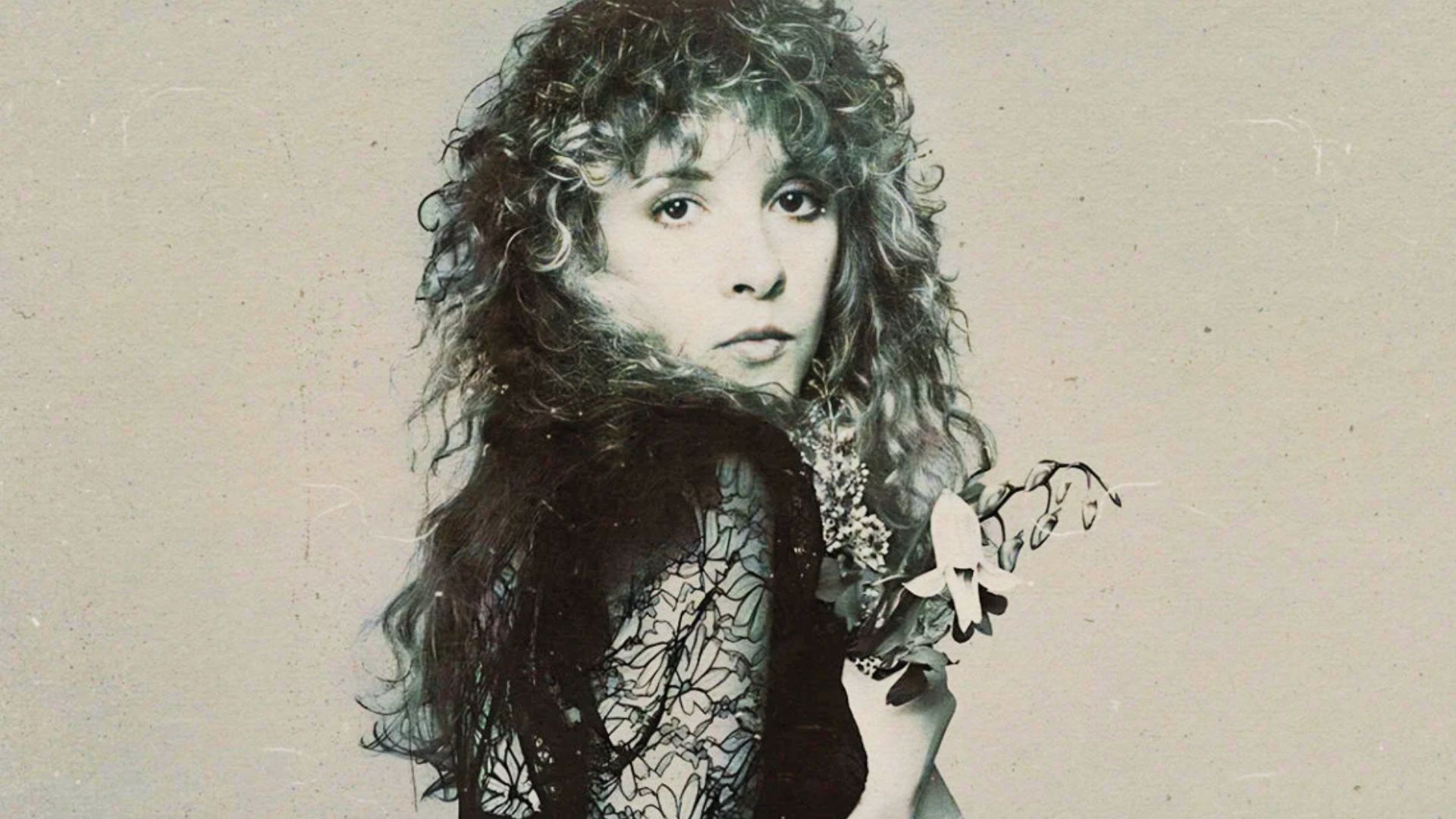 Stevie Nicks stands at an event wearing black, with long blonde curly hair and wispy bangs.