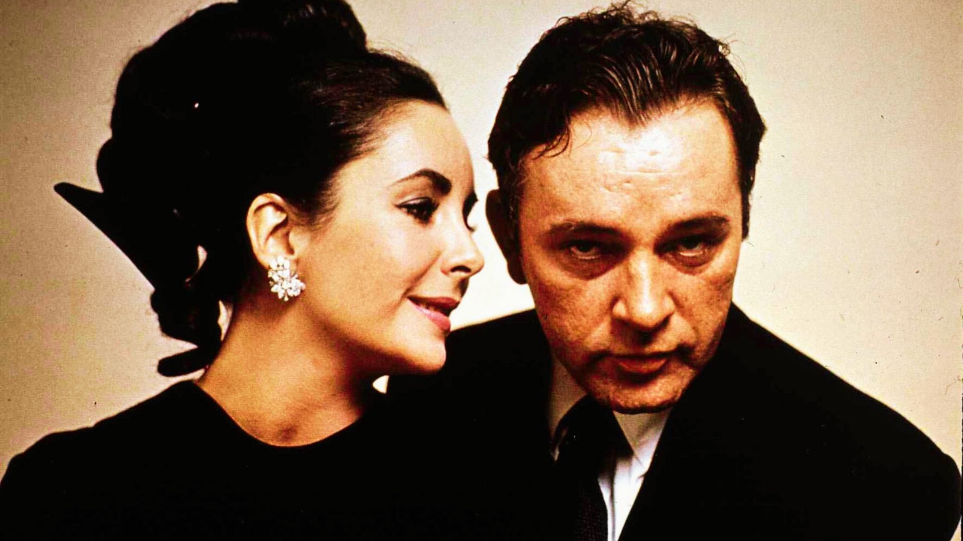 Elizabeth Taylor leans close to Richard Burton in a sleek black dress and sculptural updo.
