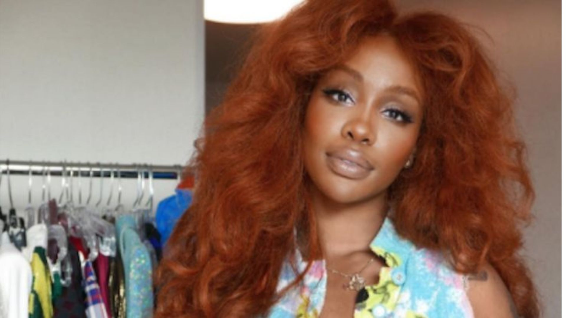 SZA with long ginger hair wearing a blue shirt, smiling at the camera.