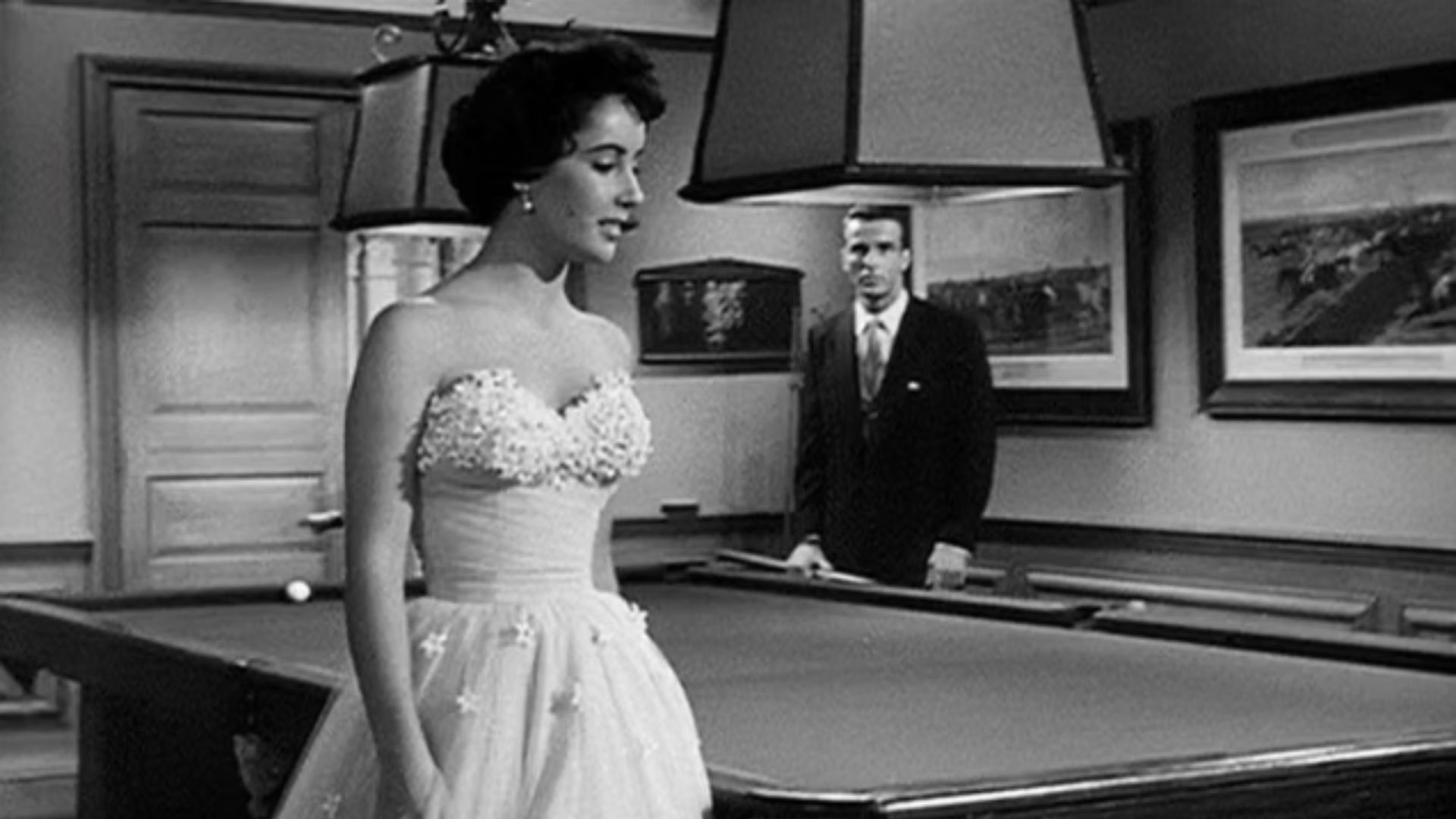 Elizabeth Taylor stands by a pool table in a strapless tulle ballgown adorned with floral appliqués.
