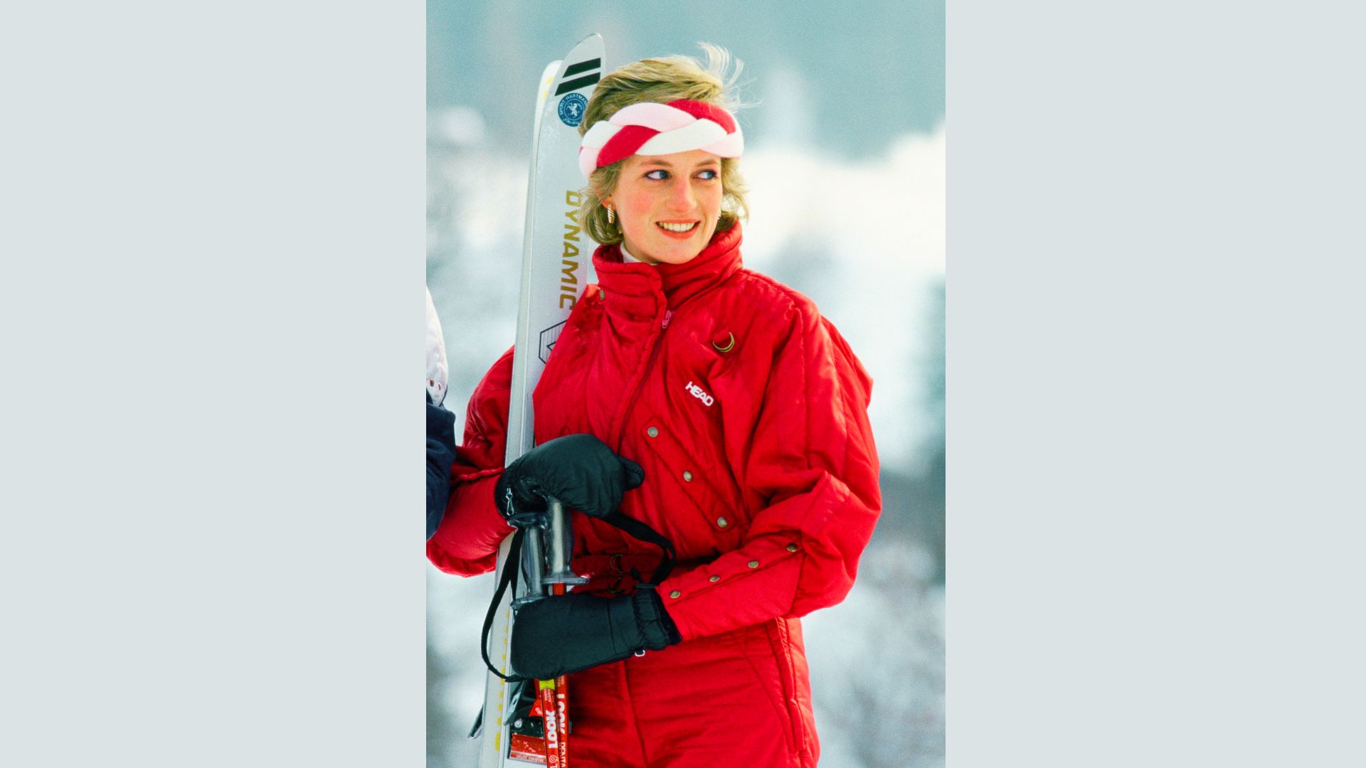 Princess Diana smiles on a ski slope in a bright Pink Head snowsuit and black gloves.