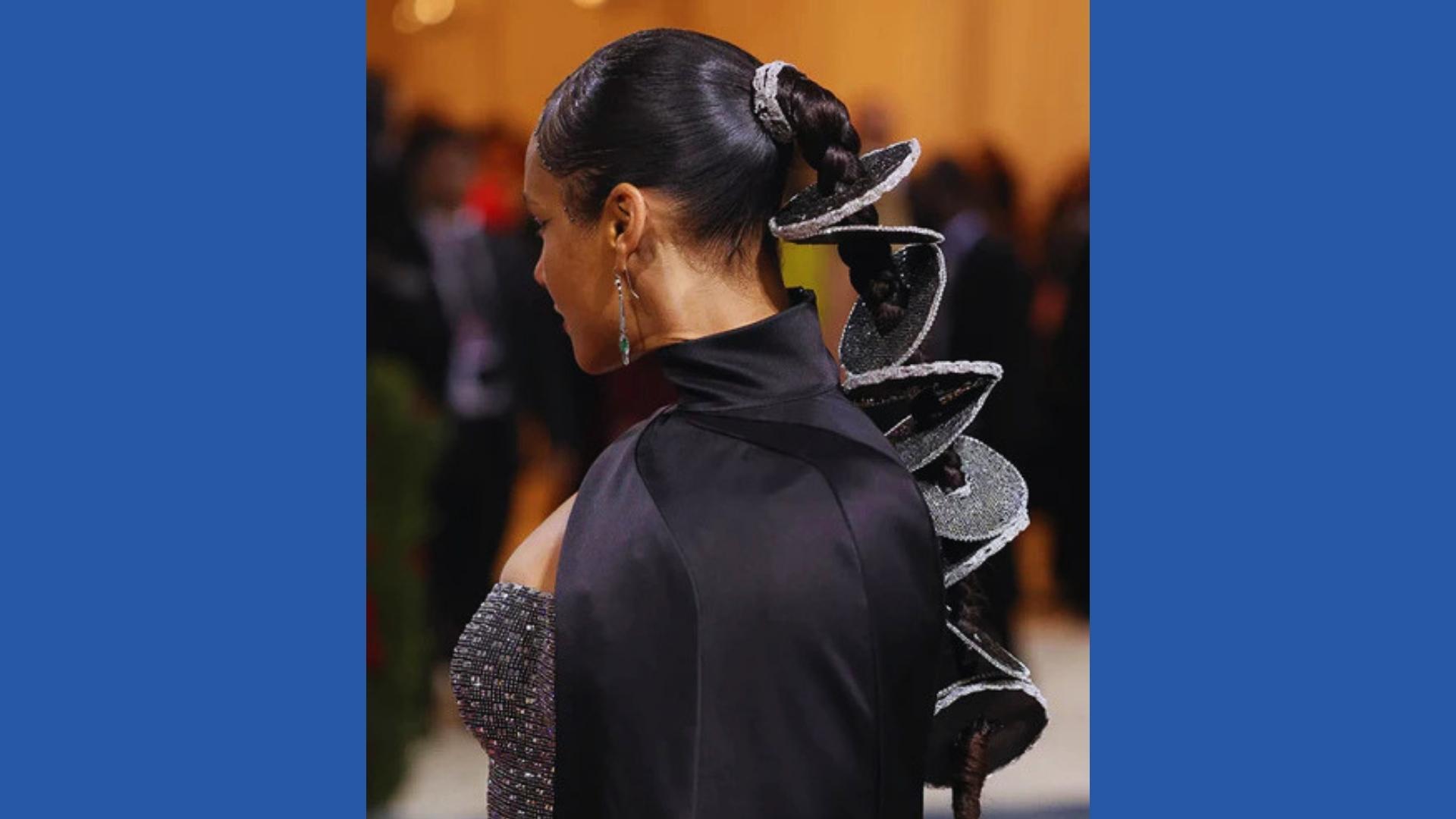 Alicia Keys at Met Gala wears sculptural braided ponytail threaded through stacked silver discs, high-neck black gown, rear view.