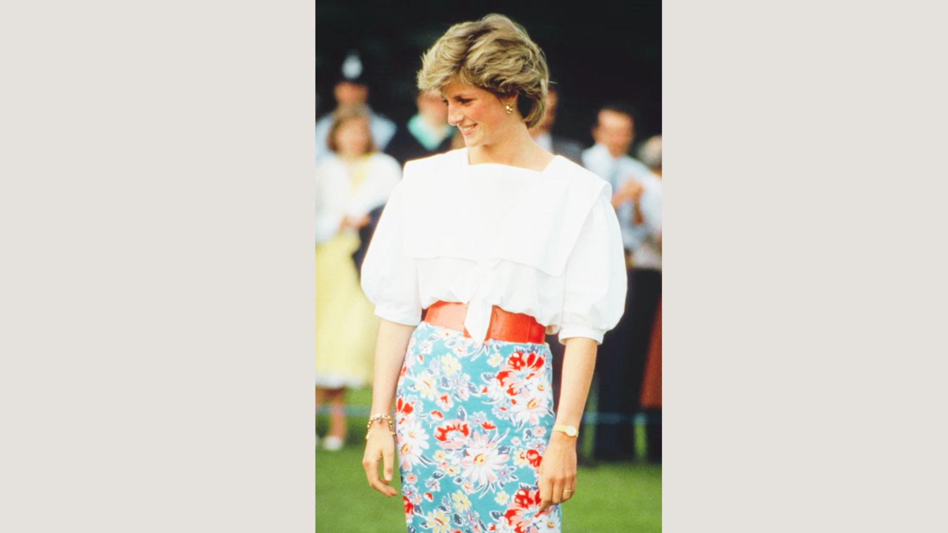 Princess Diana smiles in a white puff-sleeve blouse tied at the waist with a bold red belt.